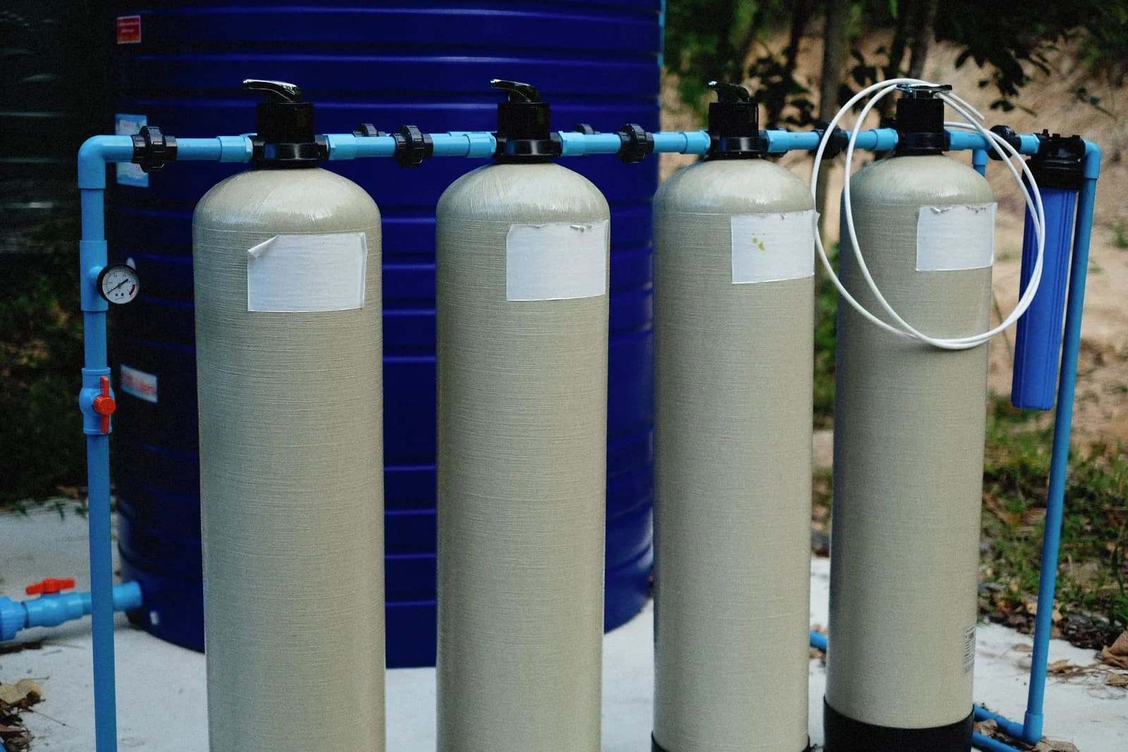 Four tall filter vessels joined by blue pipework, standing in front of a large blue water tank